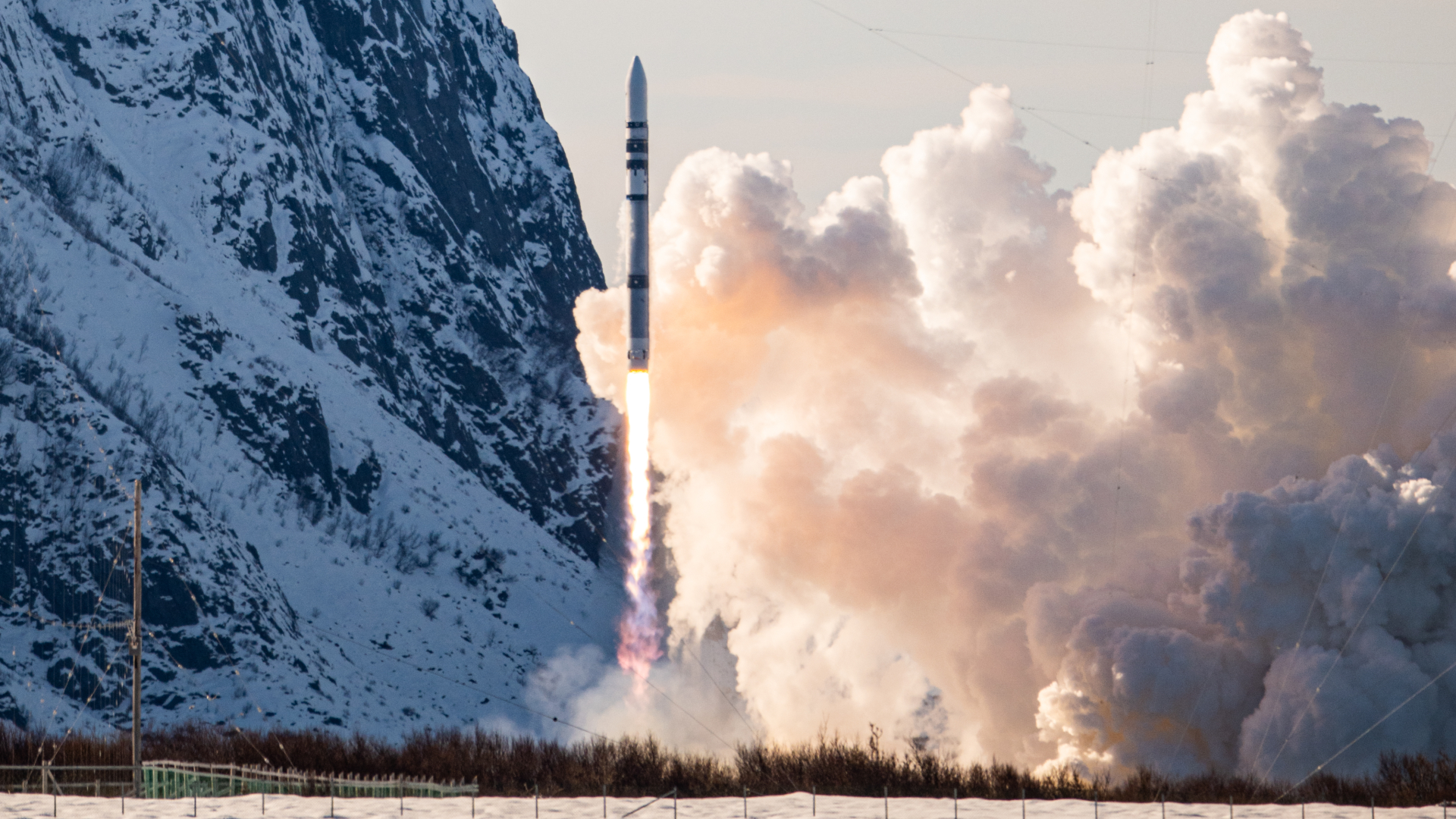 A white cylindrical rocket blasts off against a snowy landscape