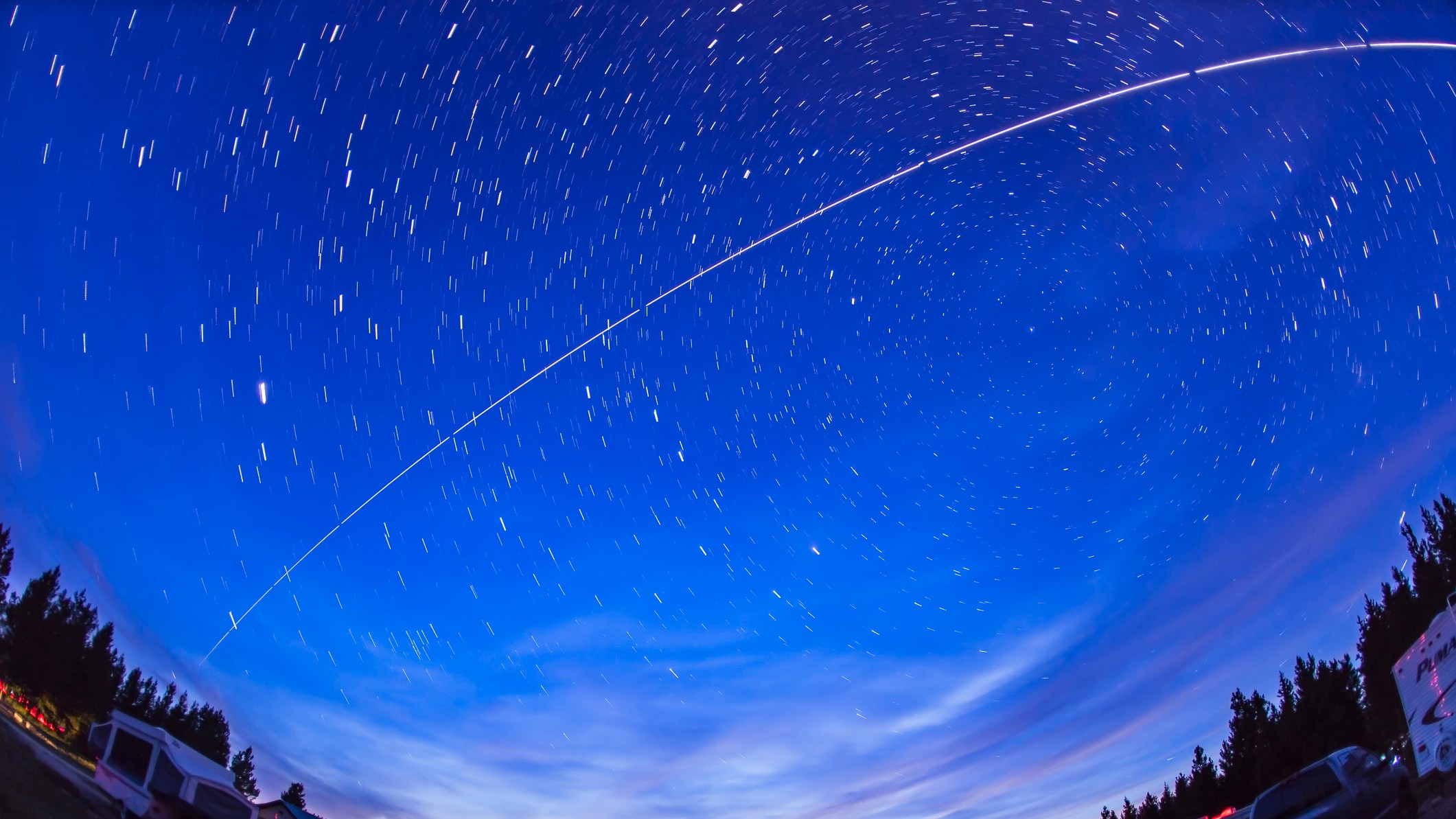 A fisheye timelapse shot of the night sky showing a streak of light representing the passage of the International Space Station.