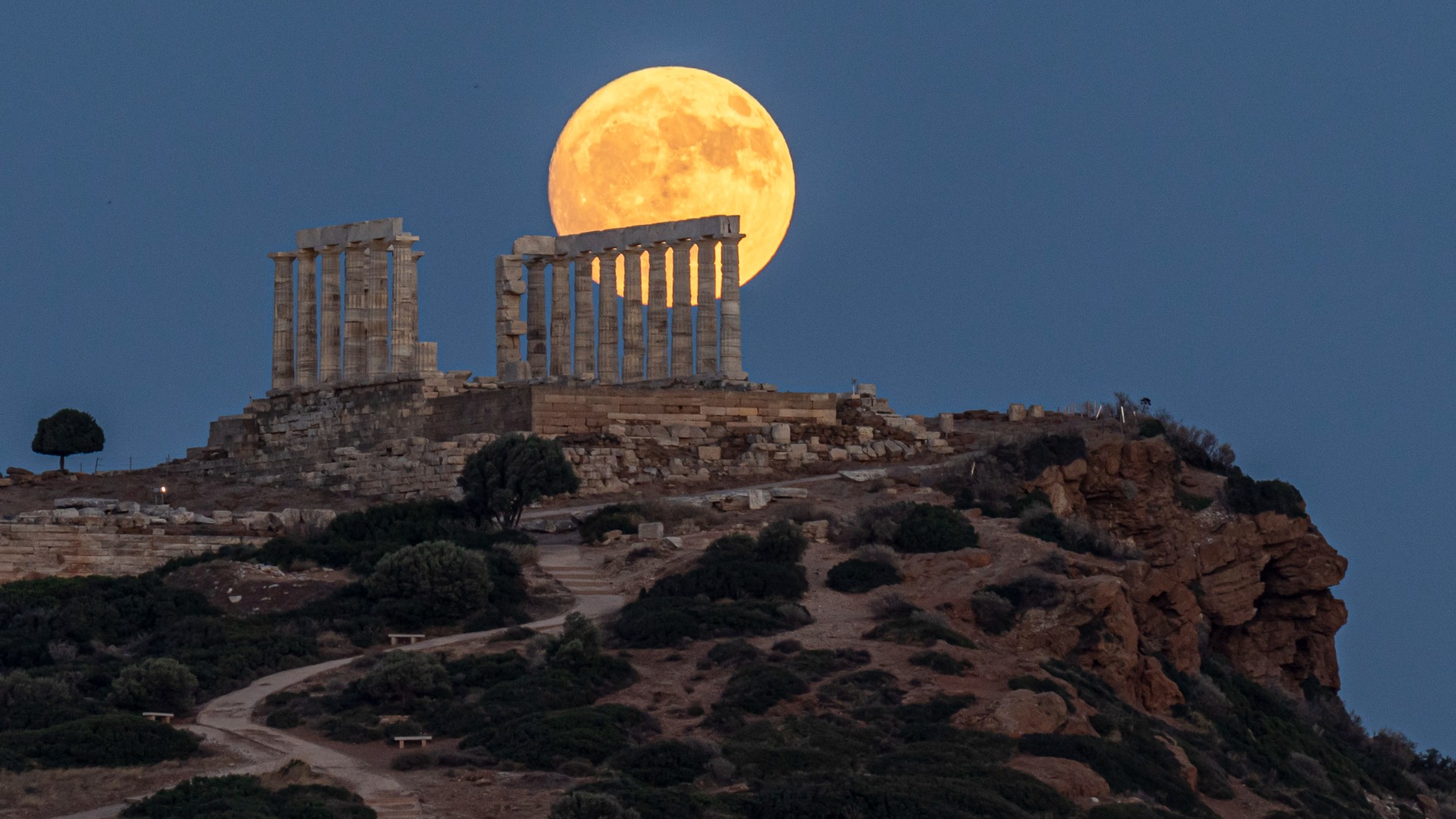 a bright, gold-colored full moon rises behind crumbling ancient ruins on a hilltop 