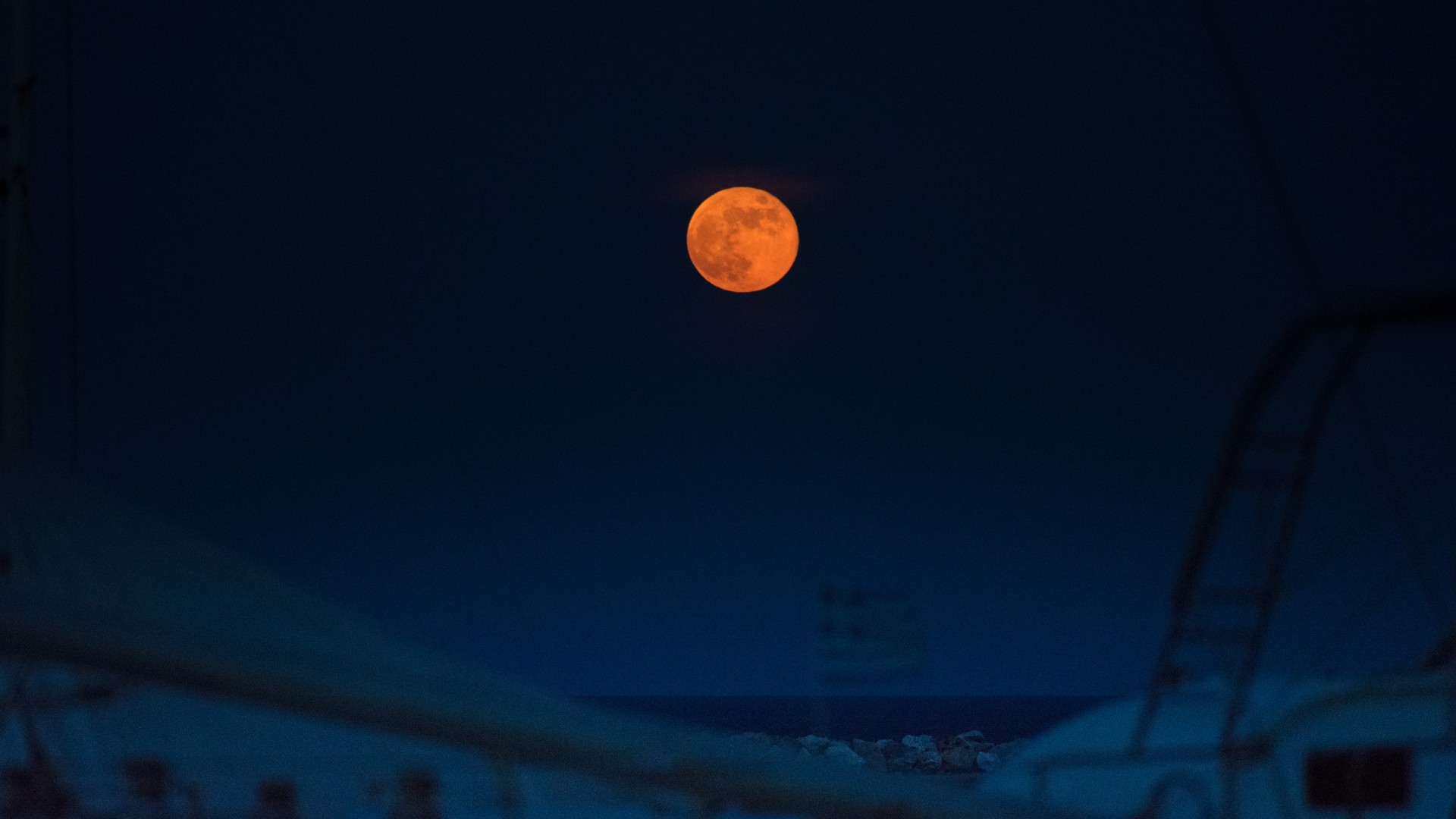 a reddish-colored moon above a seaside landscape
