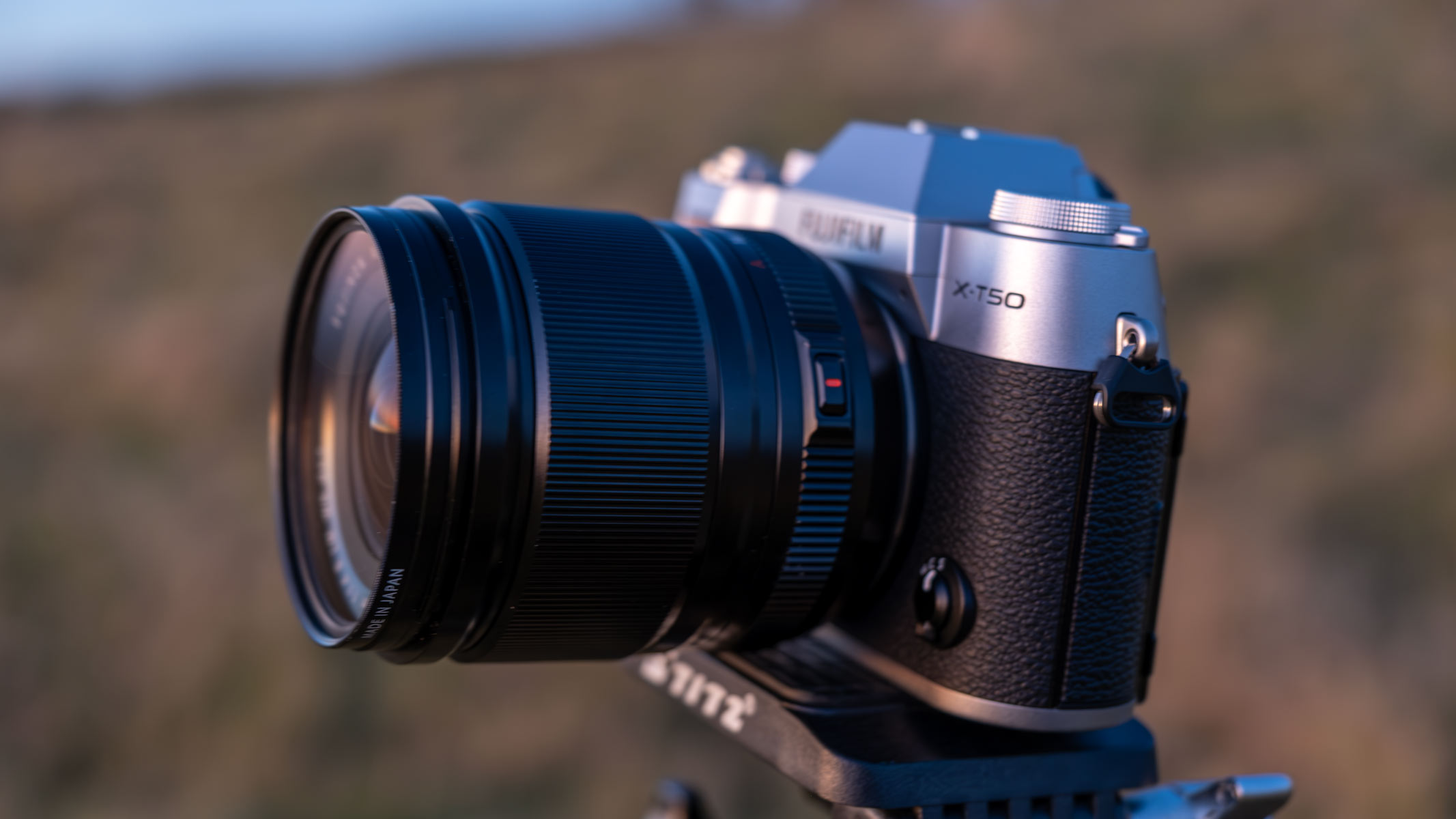 A Fujifilm X-T50 camera on a tripod in a field.