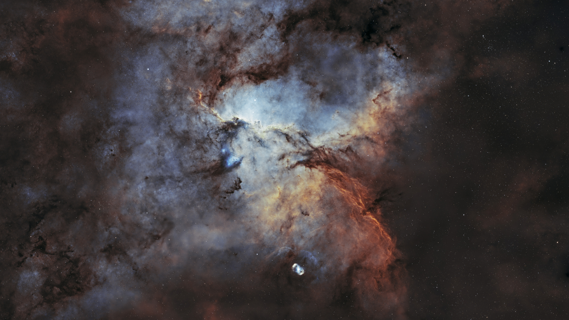 The chaotic swirling clouds of a nebula are pictured, streaked with dense filaments of cosmic dust. A darker starfield can be seen to the right of the image, while a second nebula surrounded by a ghostly shell is visible towards the bottom of the portrait.
