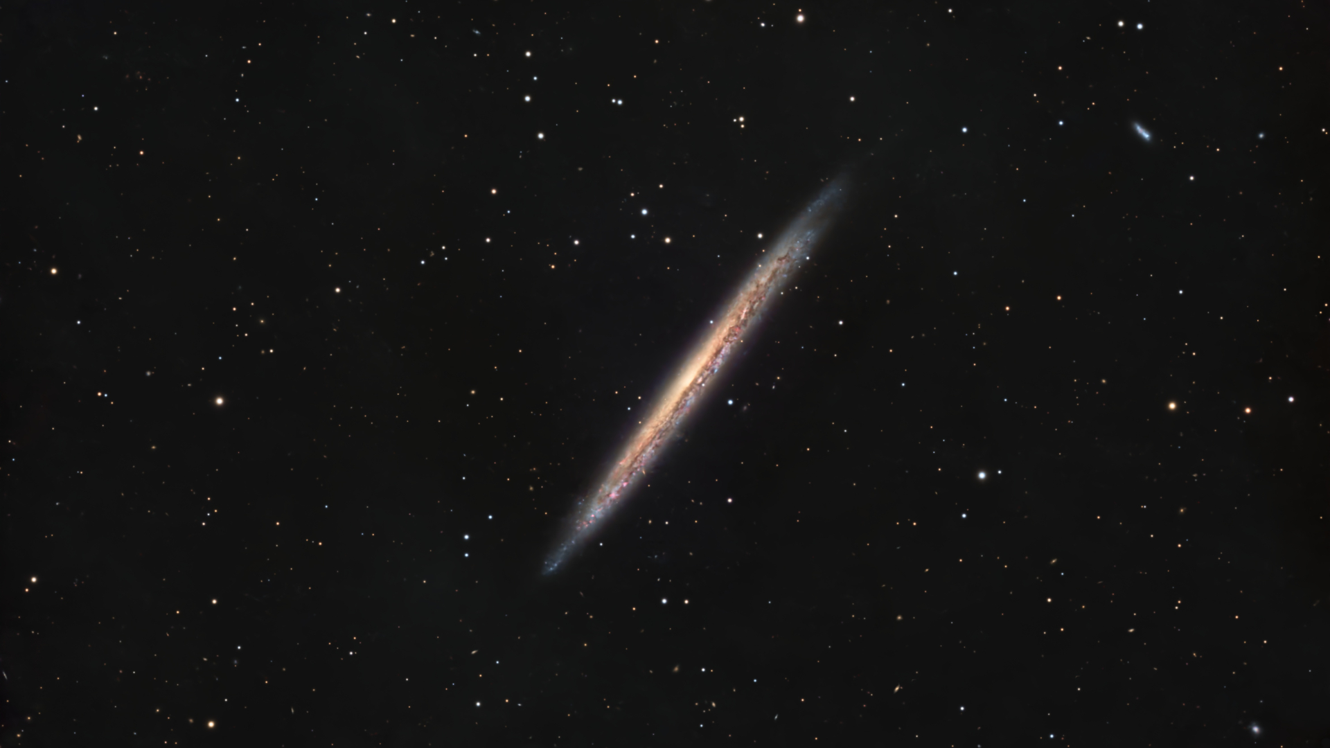 the edge-on profile of the Knife Edge Galaxy is pictured against a distant starfield on a black sky.